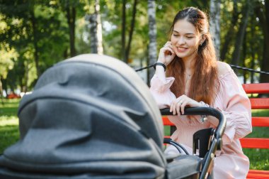 Annem bankta oturuyor. Bebek arabasında oturan bir kadın bebeğini itiyor. Aile kavramı.