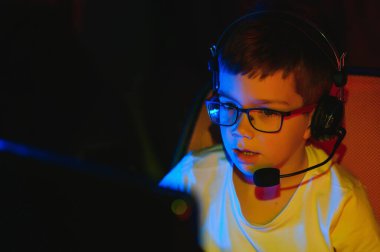 Çocuk çevrimiçi bilgisayar oyunu yayınlıyor, çocuk rgb ışıklandırma arka planında kulaklıkla yayın yapıyor