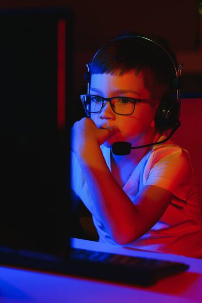 Детские онлайн трансляции компьютерных игр, мальчиковые потоки в наушниках на фоне RGB освещения