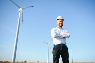 Mühendis rüzgar türbinindeki enerji üretimini kontrol ediyor. Yel değirmenindeki işçiler kaskla park eder..