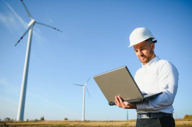 Genç mühendis tarlada rüzgar türbinlerine bakıyor ve kontrol ediyor.