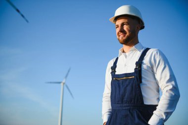 Mühendis rüzgar türbinindeki enerji üretimini kontrol ediyor. Yel değirmenindeki işçiler kaskla park eder..