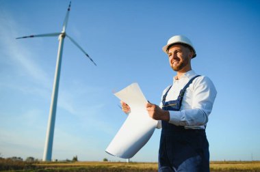 Mühendis rüzgar türbinindeki enerji üretimini kontrol ediyor. Yel değirmenindeki işçiler kaskla park eder..