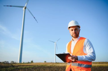 Mühendis rüzgar türbinindeki enerji üretimini kontrol ediyor. Yel değirmenindeki işçiler kaskla park eder..