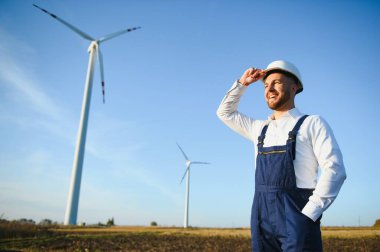 Mühendis rüzgar türbinindeki enerji üretimini kontrol ediyor. Yel değirmenindeki işçiler kaskla park eder..