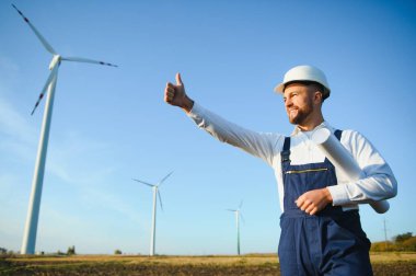 Mühendis rüzgar türbinindeki enerji üretimini kontrol ediyor. Yel değirmenindeki işçiler kaskla park eder..