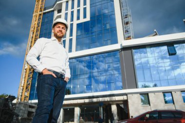 Başarılı mühendis ya da mimar, vinç ve bina inşaatı. Miğfer takan neşeli iş adamı