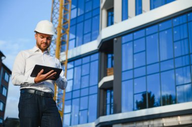 İnşaat alanındaki insan mühendisinin portresi. Beyaz kask ve sarı güvenlik yeleği giyen bir erkek inşaat müdürü.