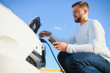 Adam şarj istasyonunda bir elektrikli arabayı şarj ediyor.
