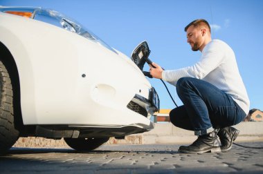 Adam şarj istasyonunda bir elektrikli arabayı şarj ediyor.