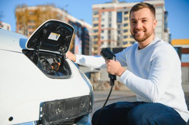 Adam şarj istasyonunda bir elektrikli arabayı şarj ediyor.