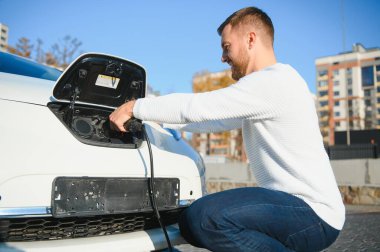 Adam şarj istasyonunda bir elektrikli arabayı şarj ediyor.