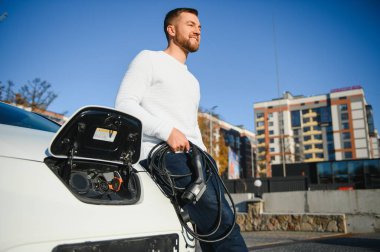 Adam şarj istasyonunda bir elektrikli arabayı şarj ediyor.