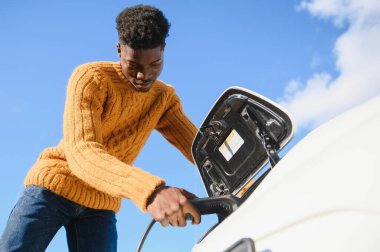 Afrikalı Amerikalı adam elektrikli arabasını şarj ediyor..