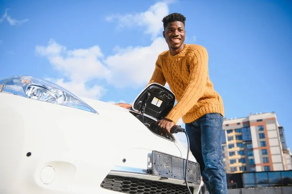 Afrikalı Amerikalı adam elektrikli arabasını şarj ediyor..