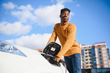 Afrikalı Amerikalı adam elektrikli arabasını şarj ediyor..