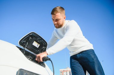 Şık bir adam elektrikli araba şarj prizine takar.