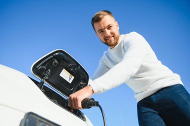 Adam şarj istasyonunda bir elektrikli arabayı şarj ediyor.