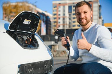 Adam şarj istasyonunda bir elektrikli arabayı şarj ediyor.