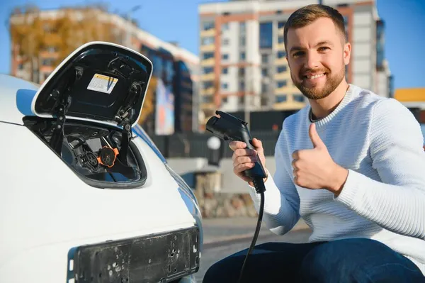 Adam şarj istasyonunda bir elektrikli arabayı şarj ediyor.