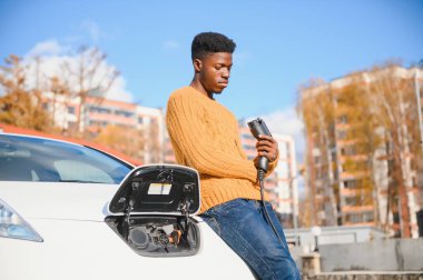 Afrikalı Amerikalı adam elektrikli arabasını şarj ediyor..