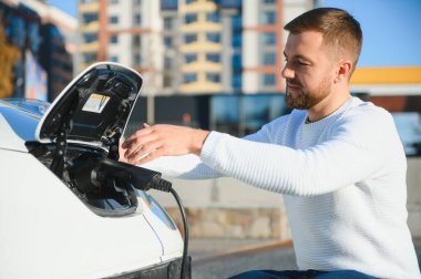 Adam şarj istasyonunda bir elektrikli arabayı şarj ediyor.