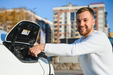 Şık bir adam elektrikli araba şarj prizine takar.