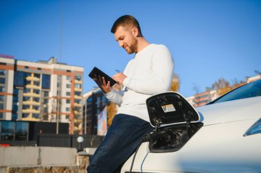 Adam şarj istasyonunda bir elektrikli arabayı şarj ediyor.