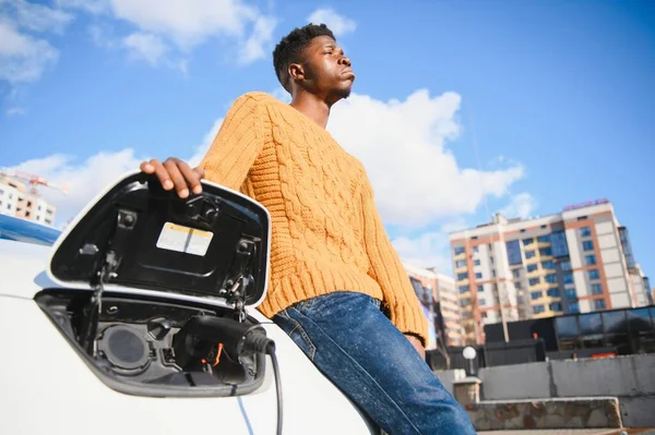 Handsome African Man Standing Luxury Charging Electric Car Talking Mobile — Stockfoto