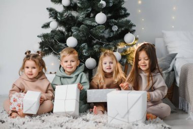Bir grup çocuk Noel sabahı arkadaşlarına hediye veriyor. Oturma odasında, arka planda, Noel ağaçlarının üzerinde oturuyorlar. Noel 'de hediye değişimi kavramı.