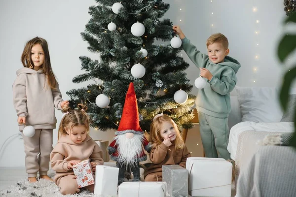 一群孩子在家里的圣诞树下 穿着华丽服装的男孩和女孩们庆祝寒假 孩子们在壁炉边打开礼物 — 图库照片