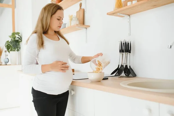 stock image pregnant woman preparing breakfast, cereals with milk and natural juice, in the kitchen.