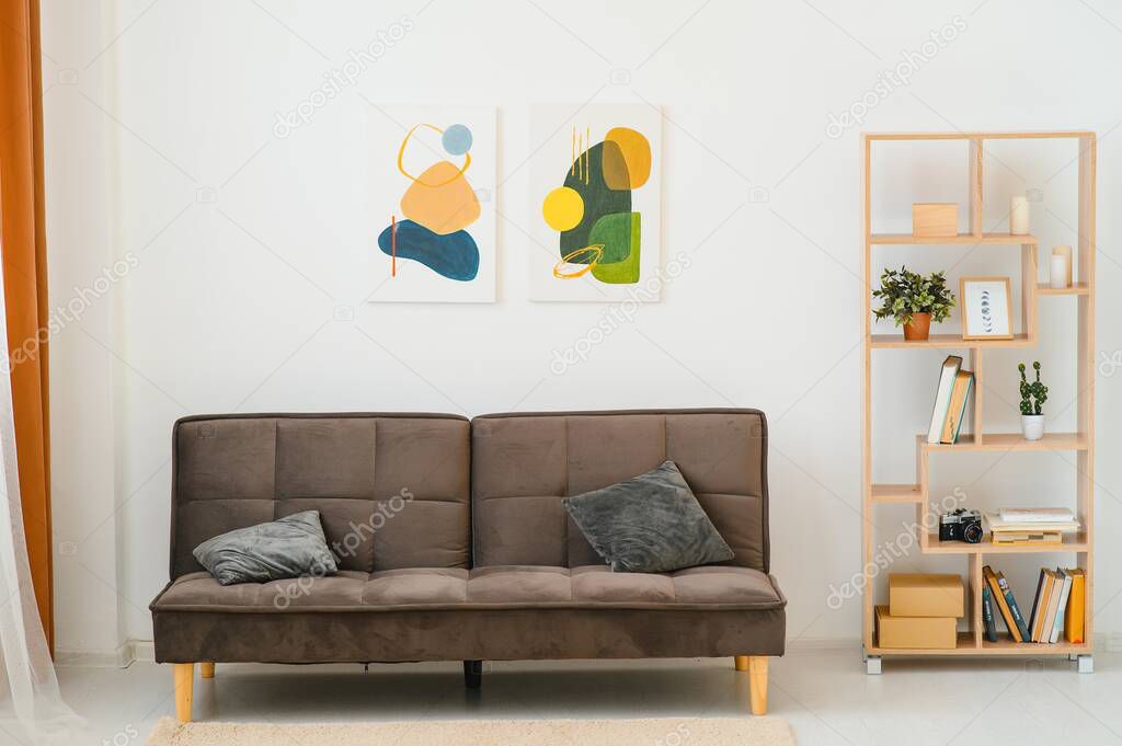 Painting on white wall above sofa with cushions in living room interior