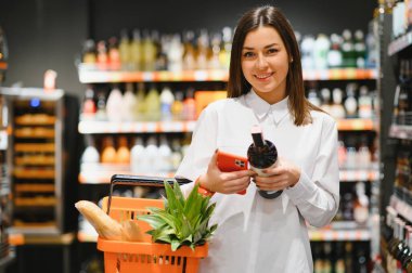 Telefonun ekranına bakarak bir süpermarkette alışveriş onun alışveriş listesi (bakkal listesi) - genç gülümseyen kadın tüketicilik ve kavram seçerek