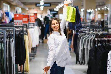 Satılık, Giysi, alışveriş, moda ve insanlar kavramı - mutlu genç kadın iki gömlek alışveriş merkezi veya giyim mağazası arasında seçme