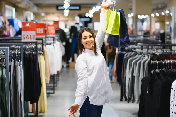 sale, clothes , shopping, fashion and people concept - happy young woman choosing between two shirts in mall or clothing store