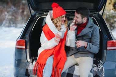 Mutlu genç çift kış ormanlarında arabanın bagajında oturmuş termostan sıcak çay içiyorlar. Kış zamanı