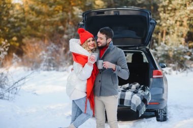 Mutlu genç çift kış ormanlarında arabanın bagajında oturmuş termostan sıcak çay içiyorlar. Kış zamanı