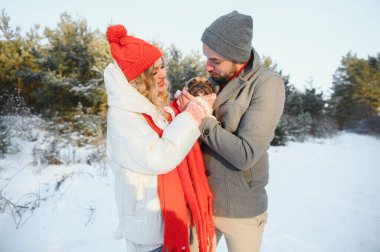 Sevgi dolu bir çift, karlı bir ormanın arka planında yürür. Bir adam bir köpek tutuyor. Beyaz ceketli ve kırmızı şapkalı bir kız..