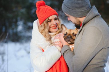 Sevgi dolu bir çift, karlı bir ormanın arka planında yürür. Bir adam bir köpek tutuyor. Beyaz ceketli ve kırmızı şapkalı bir kız..