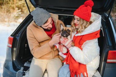 Köpekli gülümseyen bir çift karlı ormanda açık bir SUV 'nin bagajında oturuyor. Aktif kış tatillerinde birbirimizin keyfini çıkarıyoruz..