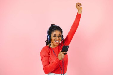 Müzik dinleme ve cep telefonuyla pembe arka plan üzerinde izole kulaklık rahat bir afro Amerikalı kadın portresi