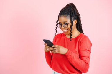 İzole edilmiş pembe arka planı olan Afrikalı Amerikalı bir kadın cep telefonuyla mesaj gönderiyor.