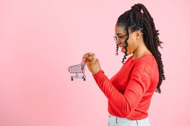 Pembe arka planda alışveriş arabası olan Afrikalı Amerikalı bir kız. Kârlı satış veya alım kavramı.