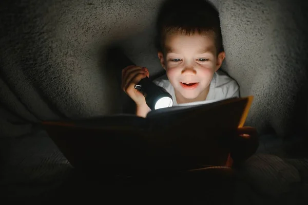 Хлопчик Ліхтариком Читає Книгу Під Ковдрою Вдома — стокове фото
