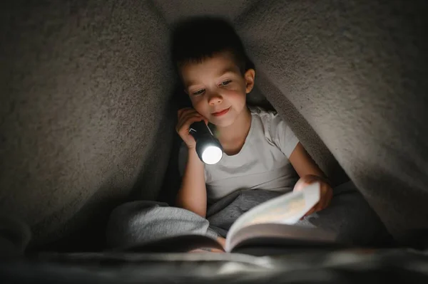 Мальчик Фонариком Читает Книгу Одеялом Дома — стоковое фото