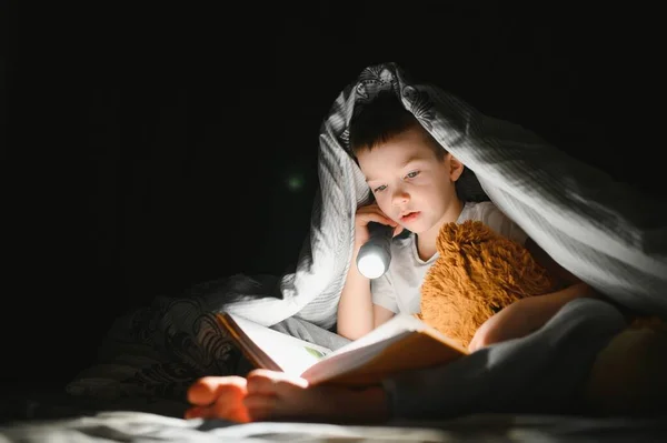 Хлопчик Ліхтариком Читає Книгу Під Ковдрою Вдома — стокове фото