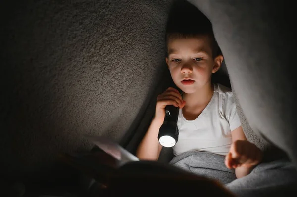 Мальчик Фонариком Читает Книгу Одеялом Дома — стоковое фото