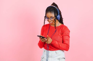 Müzik dinleme ve cep telefonuyla pembe arka plan üzerinde izole kulaklık rahat bir afro Amerikalı kadın portresi