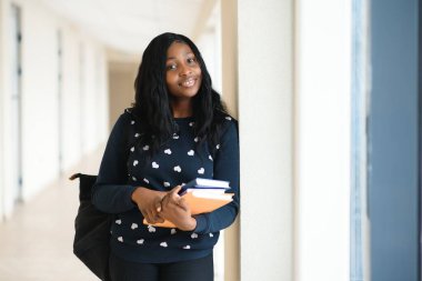 Genç Afrikalı Amerikalı öğrenci kampüste mutlu bir şekilde yürürken gülümsüyor..